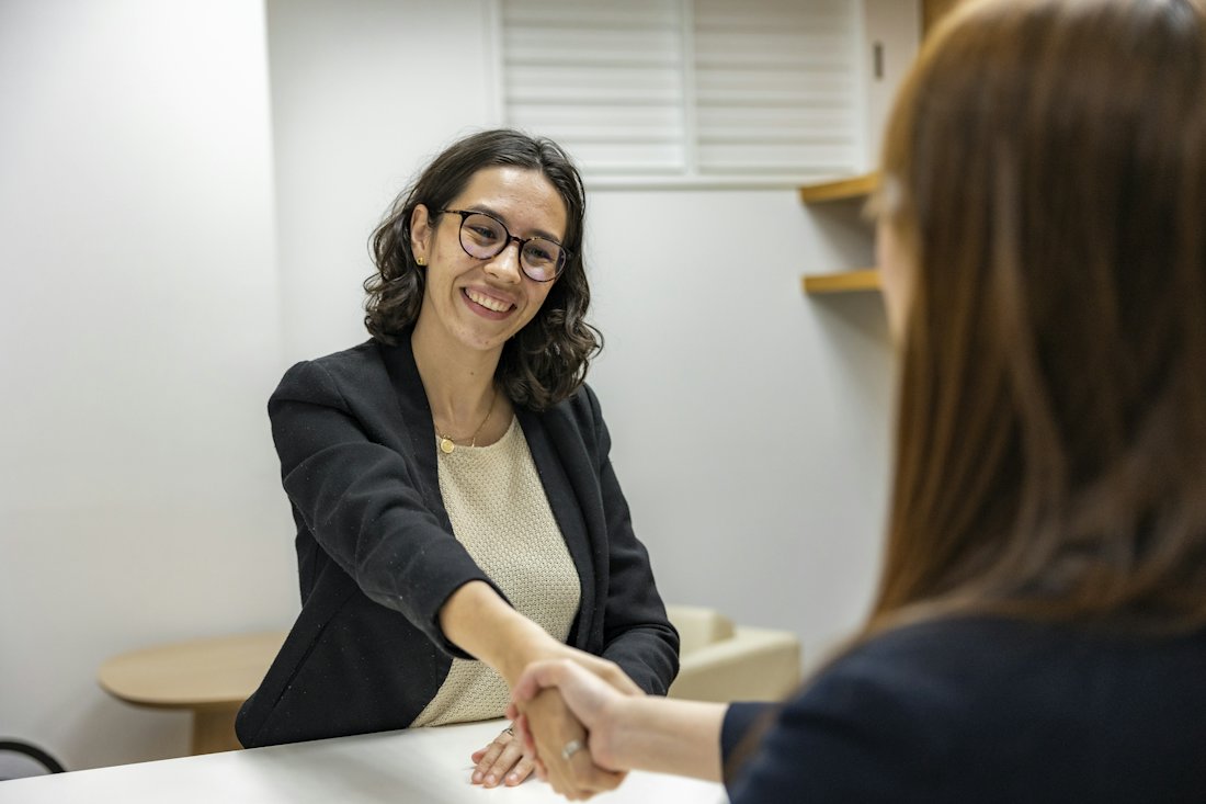 Broker smiling and shaking hands with a client across a desk